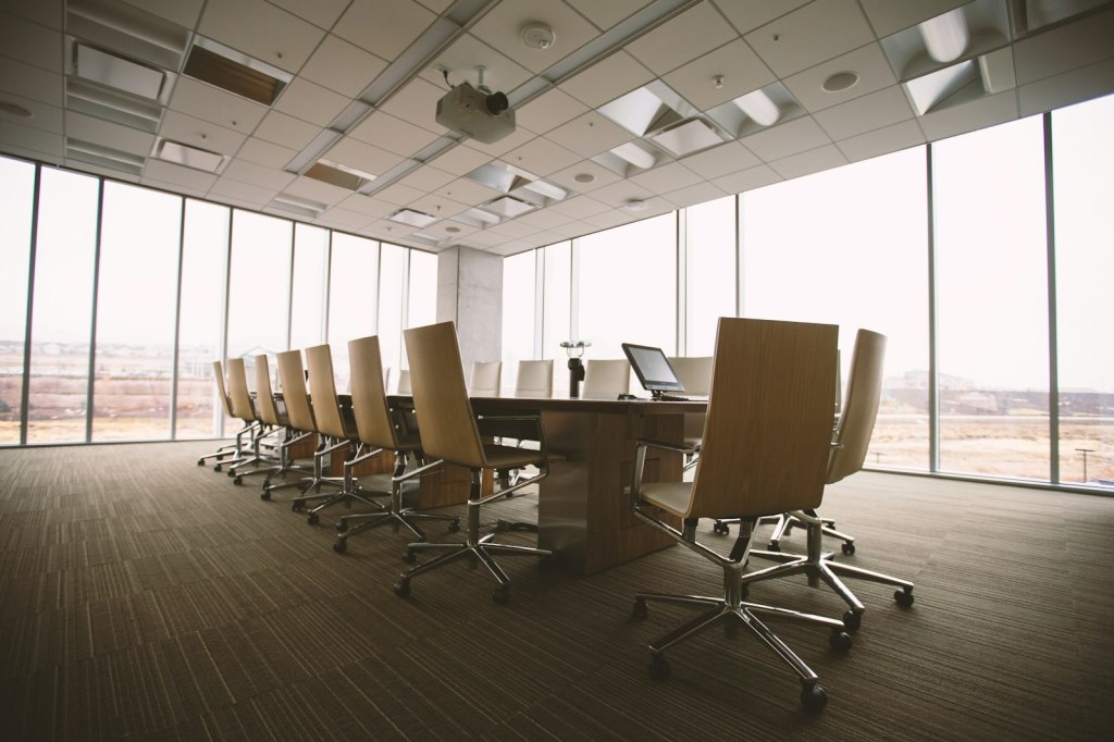 Une salle de conseil vide : grande table ovale en bois entourée de fauteuils, prête pour la séance.