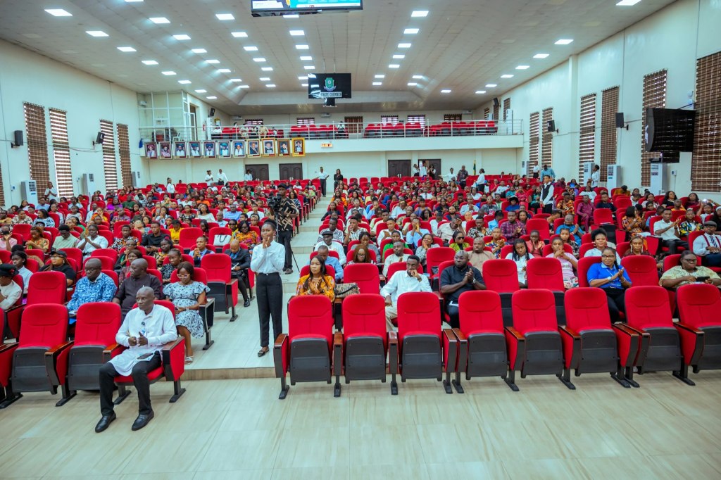 Une salle d'assemblée aux fauteuils rouges, remplie de participants.